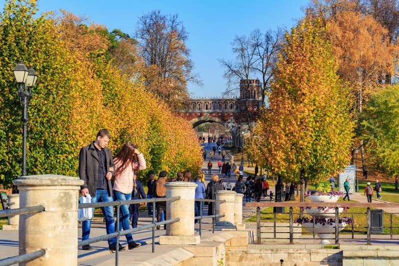 Moscow, Russia - October 17, 2018: Tourists walking on alley among trees with golden leaves at sunny autumn day in Tsaritsyno park in Moscow