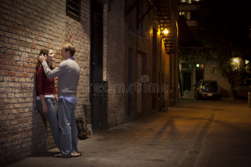 Couple leaning against brick wall in alley way at night time. Couple leaning against brick wall in alley way at night time