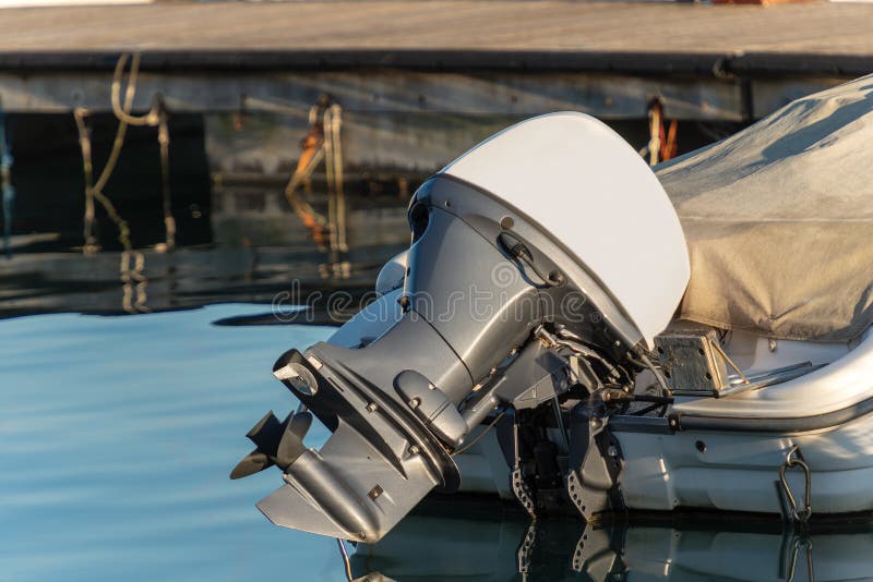 Detail of one outboard motor engine and propeller, on a boat moored in the port with reflections. Detail of one outboard motor engine and propeller, on a boat moored in the port with reflections