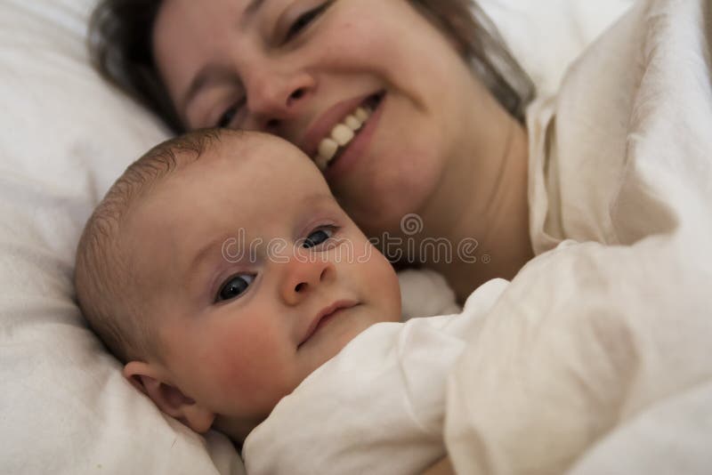 La madre e il bambino felicemente sdraiato, in crema letto guardando la telecamera.