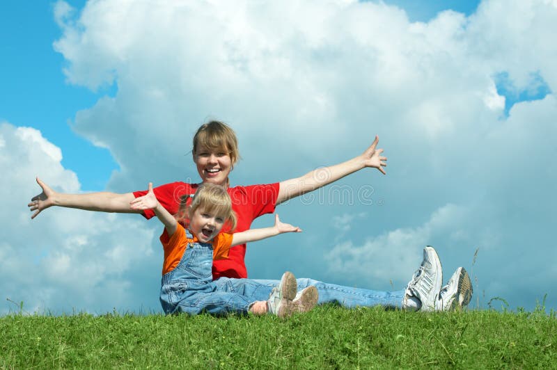 Mother and baby sit on grass and open wide hand