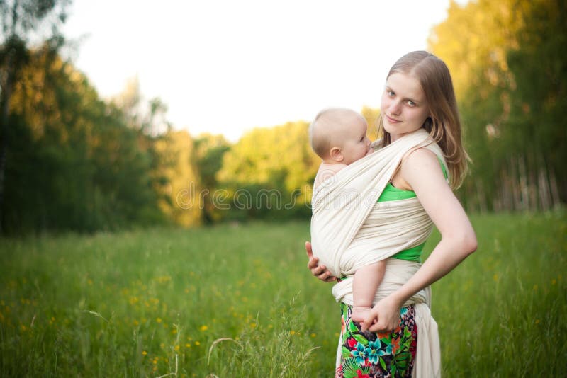 Mother carrying daughter in sling in field