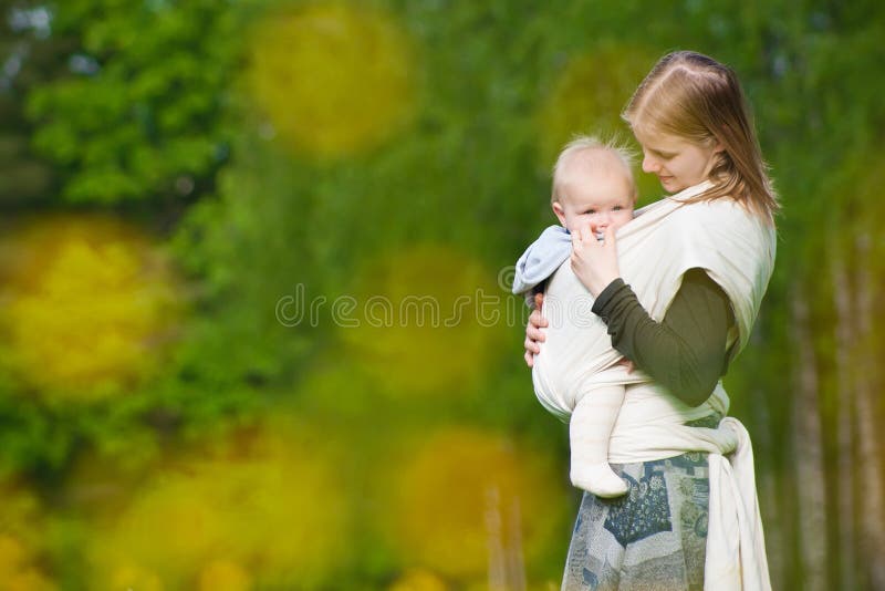 Mother carrying daughter in sling in park