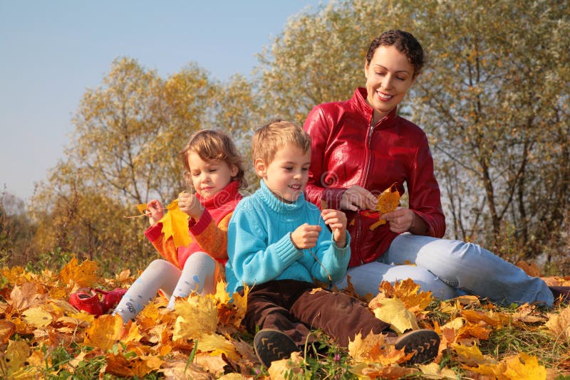 Mother with children sit on fallen maple leaves