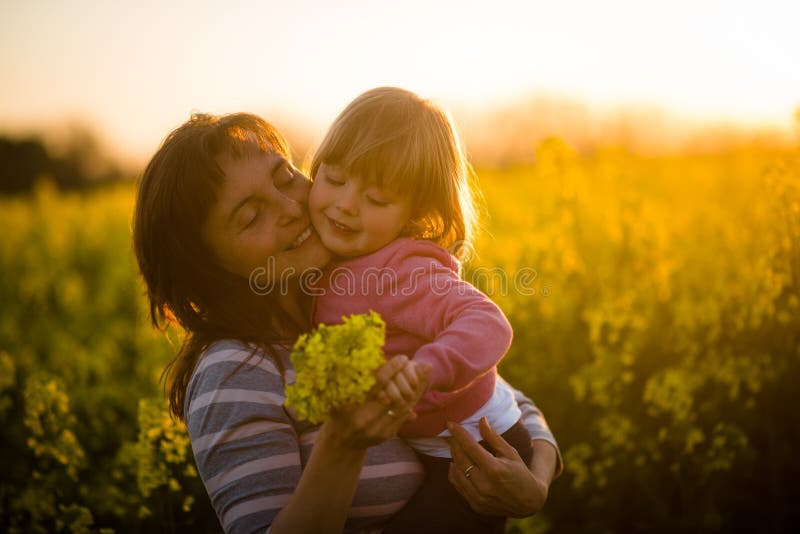 Mother with cute smiling daughter in the rapeseed field during sunset stock images Mother with cute smiling daughter in the rapeseed field during sunset stock images