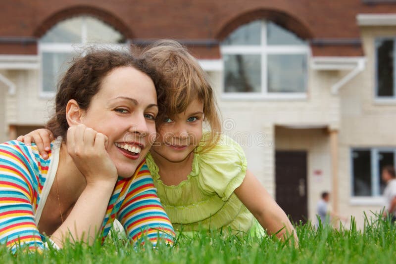 Mother and daughter lying on lawn in front of home