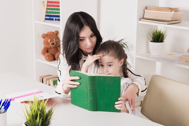 Mother and daughter reading time. Learning together sitting at the table. stock photography