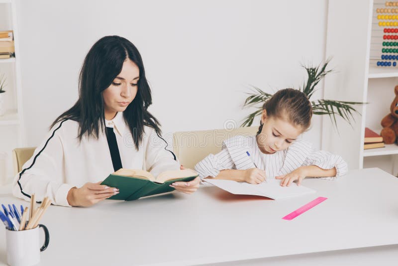 Mother and daughter reading time. Learning together sitting at the table. stock image