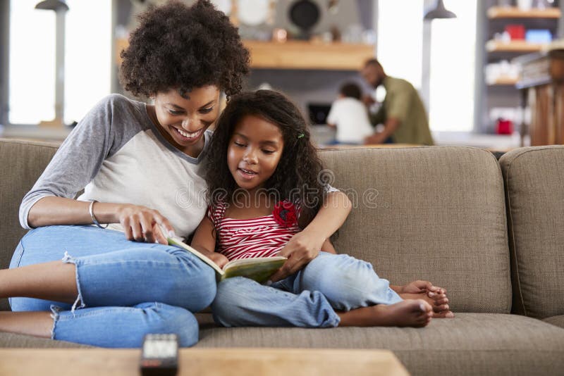 Mother And Daughter Sit On Sofa In Lounge Reading Book Together stock photos Mother And Daughter Sit On Sofa In Lounge Reading Book Together stock photos