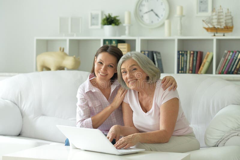 Mother and daughter sitting at table with laptop, at home