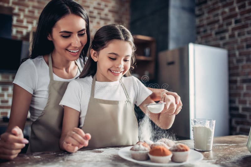 Mother and daughter sprinkling with sugar powder cupcakes