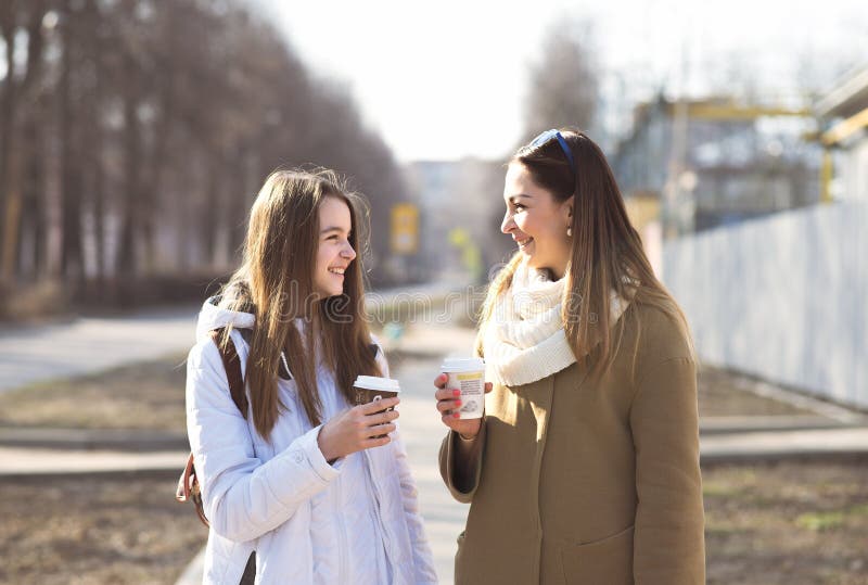 Mother and daughter talking, laughing smiling on the street, drinking coffee in cups