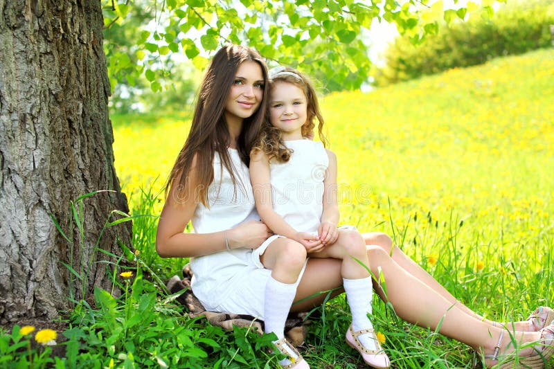 Mother and daughter together on the grass near tree in summer