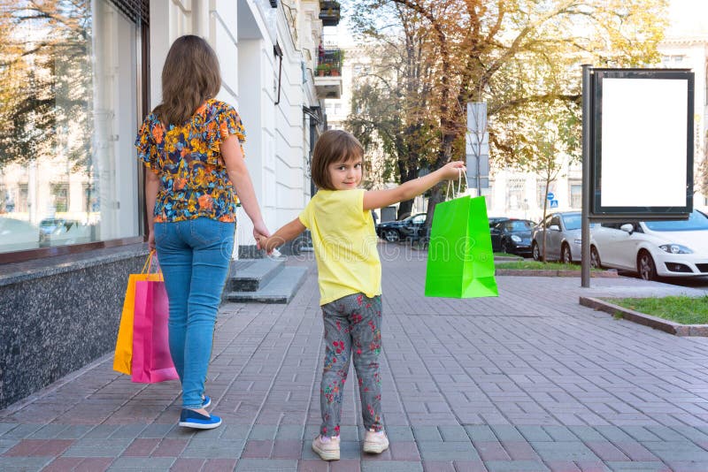 A mother and daughter walk along the street with purchases, kind from a bac...