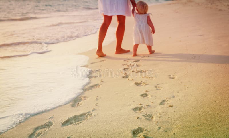 Mother and daughter walking on beach leaving footprint in sand