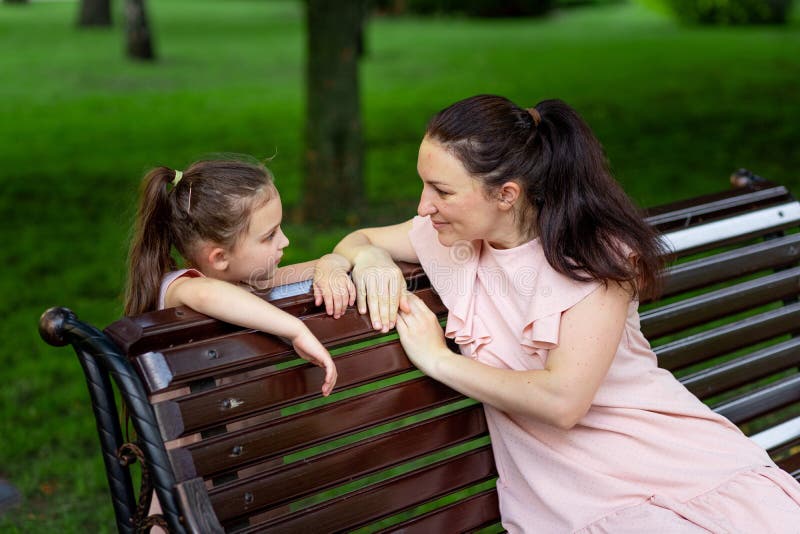 Mother and daughter 5-6 years old walking in the Park in the summer, mother talking to her daughter sitting on a bench, the stock images