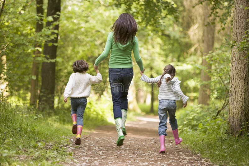 Mother and daughters skipping on path smiling.