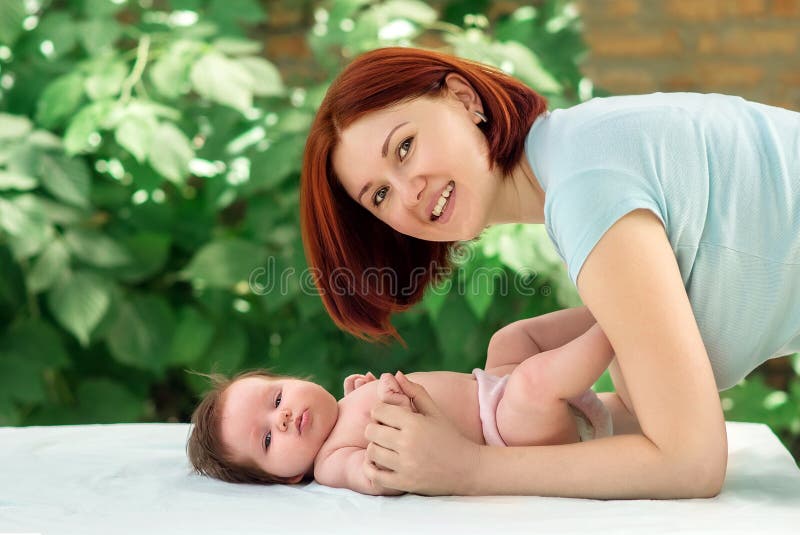 Mother doing exercises for infant daughter in garden, baby receiving air bath under guidance of mom. Health hardening for babies