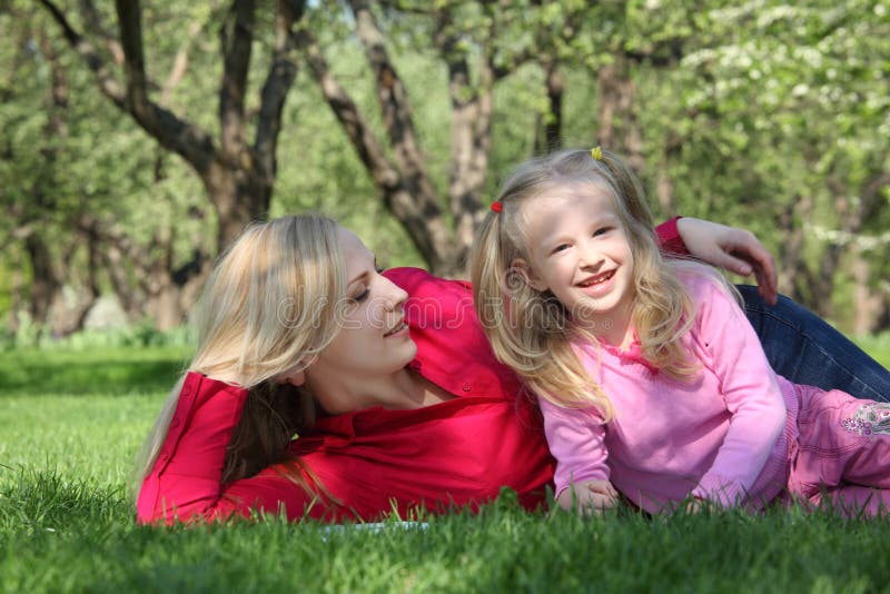 Mother embraces daughter lying on grass