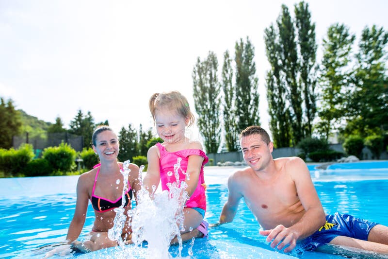 Mother, father and daughter in swimming pool. Sunny summer.