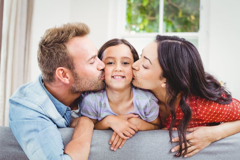 Mother and father kissing daughter at home stock photography.