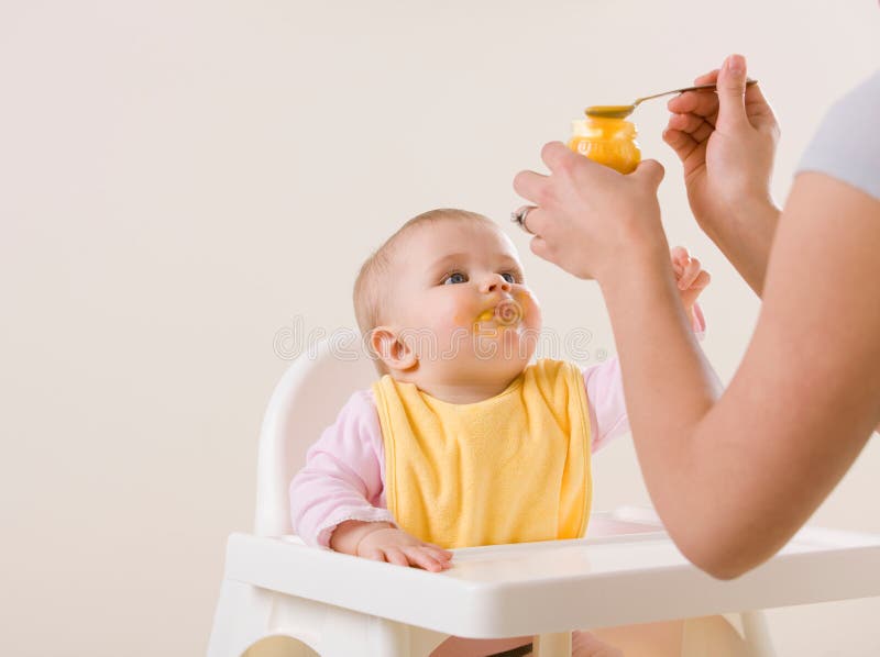 Mother feeding hungry baby in highchair