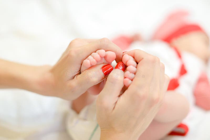 Mother gentle hands with red nails holding newborn baby legs.