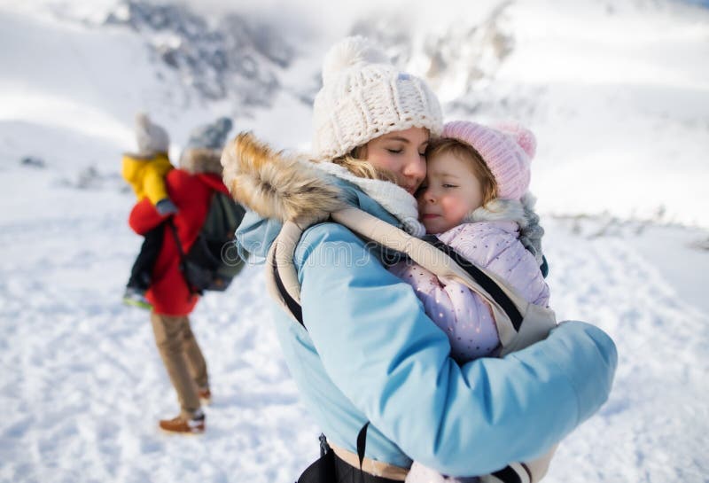 Mother with happy small daughter in carrier standing in winter nature, resting.