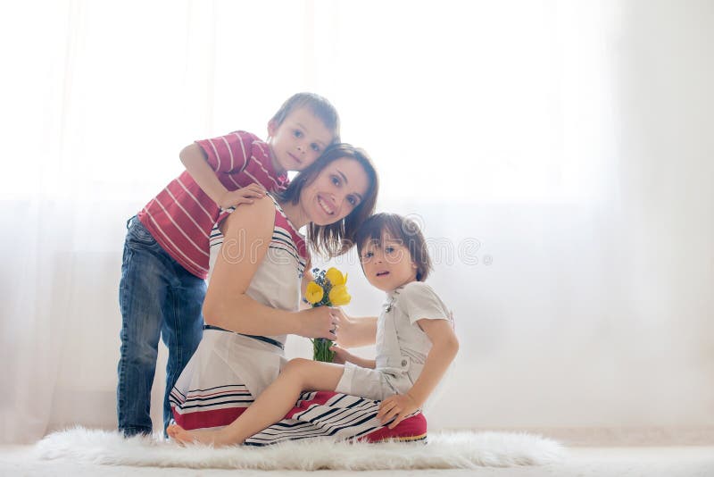 Mother and her beautiful childnren embracing with tenderness and care, child giving mother flowers. Mother day concept, happiness and love. Mother and her beautiful childnren embracing with tenderness and care, child giving mother flowers. Mother day concept, happiness and love