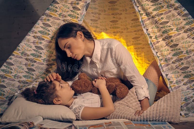 Mother and her daughter are in a teepee tent with some pillows. Happy family. stock photo Mother and her daughter are in a teepee tent with some pillows. Happy family. stock photo