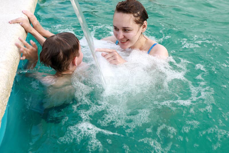 Mother with her son playing under stream of water in pool stock photography