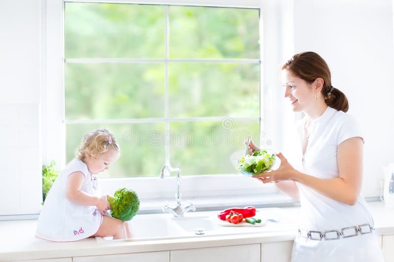 Mother and her toddler daughter cooking healthy salad