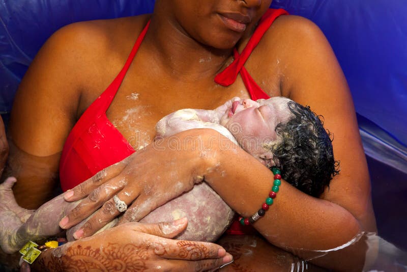 Americano madre adaptadores su bebé recién nacido después dar nacimiento sobre el en maternidad piscina de Agua.