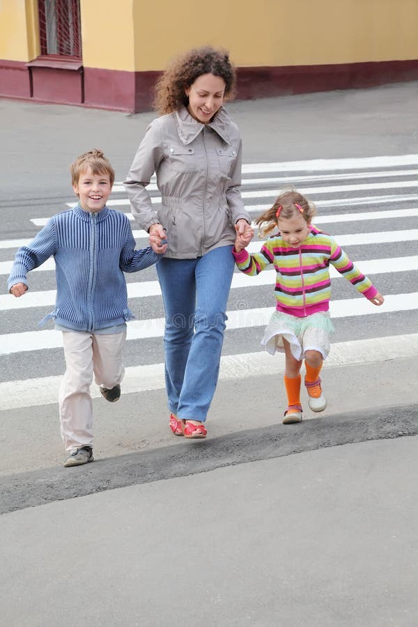 Mother holds hand of children and crossing road