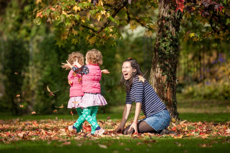 Mother and identical twins having fun with autumn leaves in the park, blond cute curly girls, happy kids, girls in pink jacket stock photo Mother and identical twins having fun with autumn leaves in the park, blond cute curly girls, happy kids, girls in pink jacket stock photo