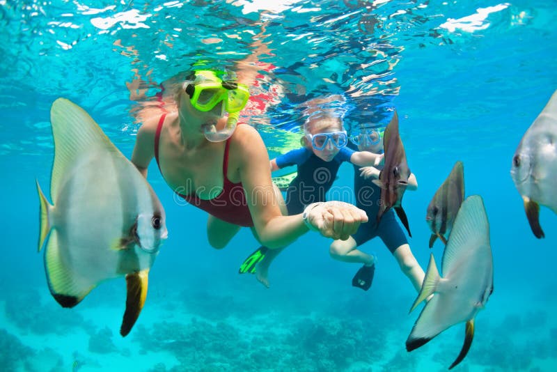 Mother, kid in snorkeling mask dive underwater with tropical fishes