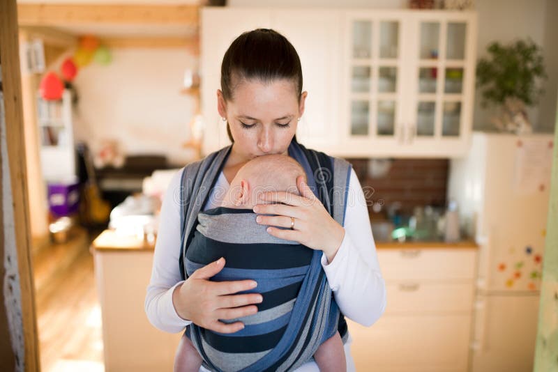 Mother in kitchen with her son in sling, kissing him