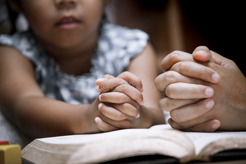 Mother and little girl hands folded in prayer on a Holy Bible