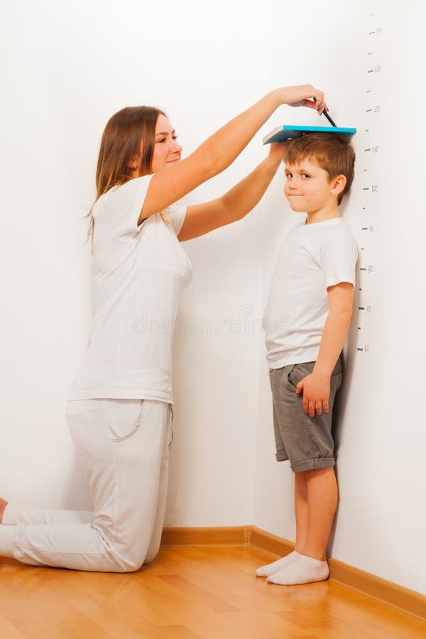 Madre medición su hijos altura contra blanco muro, muestra línea bolígrafo, cómo un nino de pie sobre el piso.