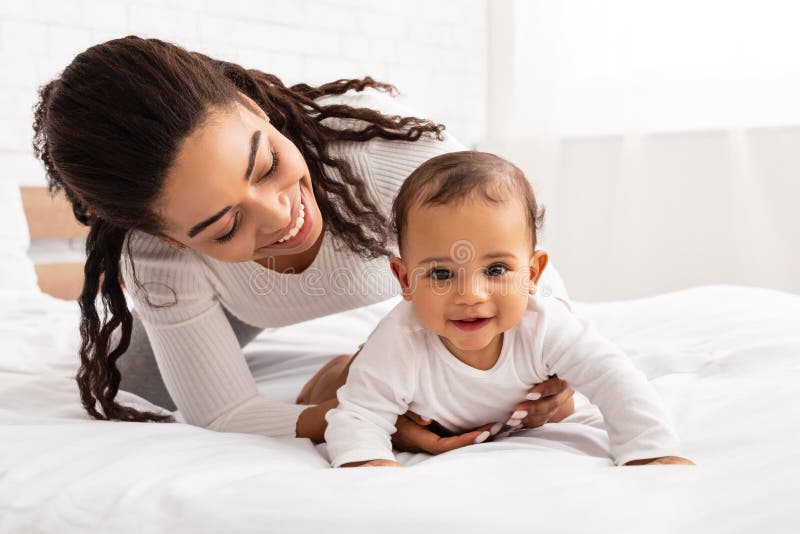 Mother Playing With Baby Helping Her Crawl On Bed Indoor