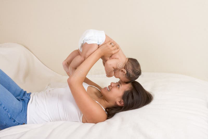 Mom and son on bed and mother embracing the infant baby playing with him. Happy multiethnic boys stock images, royalty-free photos and pictures