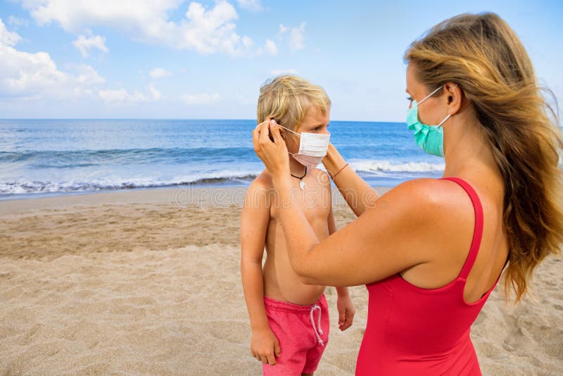 Mother put medical mask on child on sea beach. New rules to wear cloth face covering at public places. Cancelled cruise, tour due coronavirus COVID 19. Family vacation, travel lifestyle at summer 2020. Mother put medical mask on child on sea beach. New rules to wear cloth face covering at public places. Cancelled cruise, tour due coronavirus COVID 19. Family vacation, travel lifestyle at summer 2020