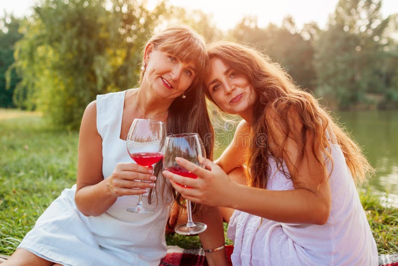 Mother`s day. Mother drinking wine with her adult daughter in spring park. Family having picnic outdoors