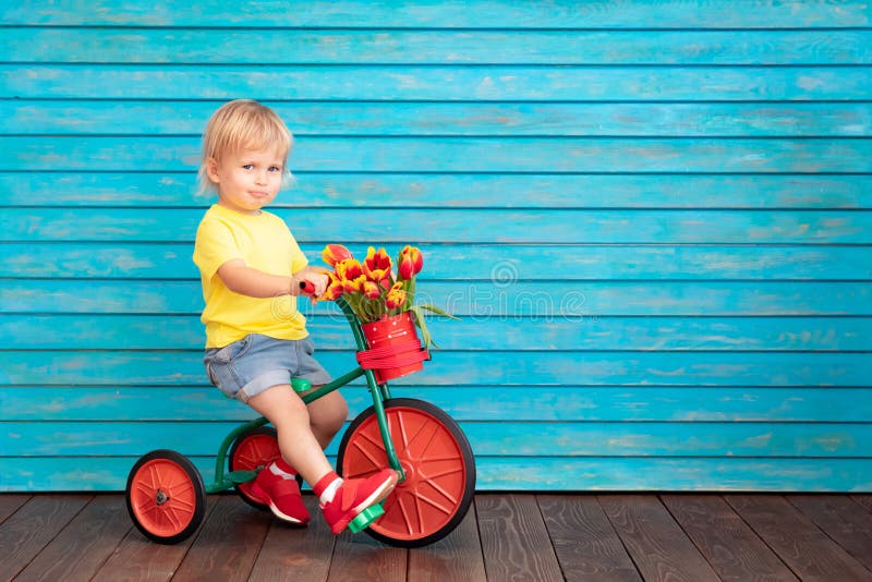 Funny child riding bike. Happy kid having fun at home. Spring family holiday concept. Mother`s day. Funny child riding bike. Happy kid having fun at home. Spring family holiday concept. Mother`s day