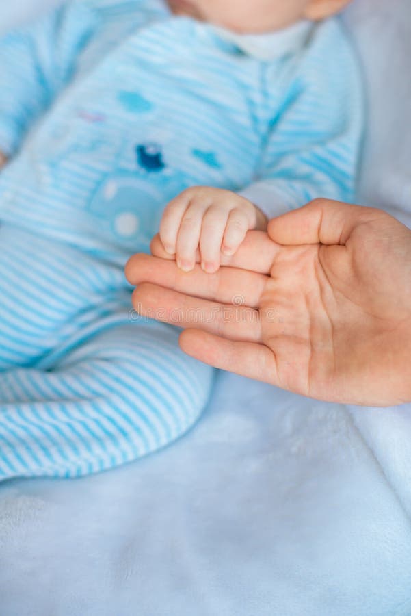 Mother`s hand holds a cute little baby in her hand at home on the bed stock photo Mother`s hand holds a cute little baby in her hand at home on the bed stock photo