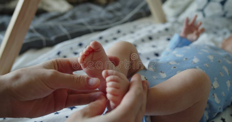Mother's hands holding newborn baby's feet lying on his back on the bed stock video footage