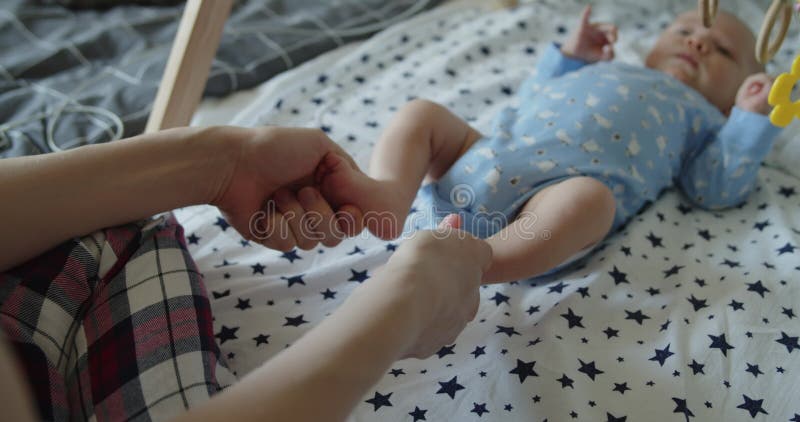 Mother's hands holding newborn baby's feet lying on his back on the bed stock video