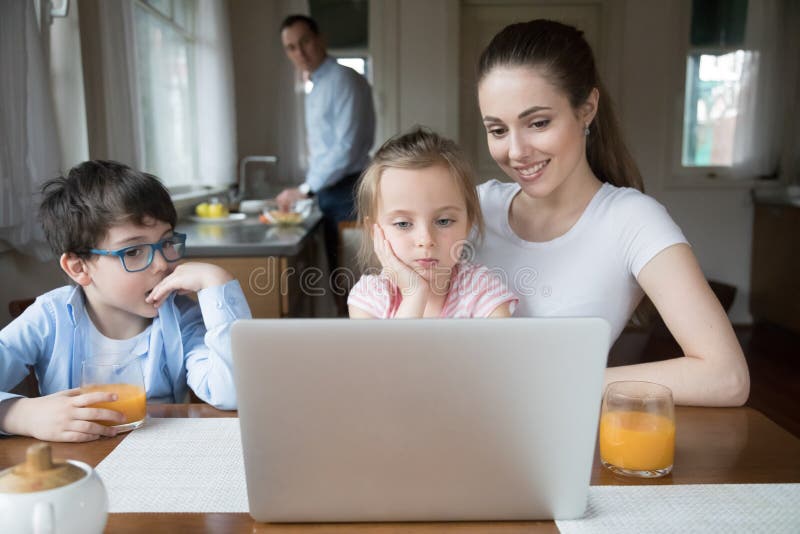 Mother showing cartoon on computer for children while father cooking. Family having fun, relax, leisure time on weekend at home. Wife entertaining kids. Gadget addiction concept, bad eyesight problem