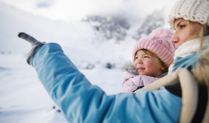 Mother with small daughter in carrier standing in winter nature, talking.