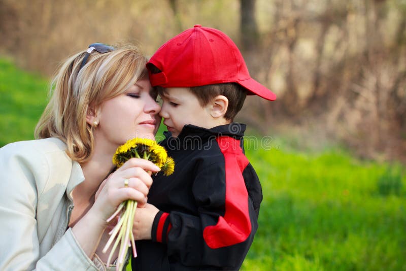 Cute little boy in red cap gives yellow dandelion to mother at outdoor. Cute little boy in red cap gives yellow dandelion to mother at outdoor